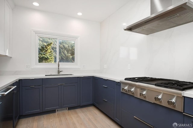 kitchen featuring stainless steel gas stovetop, wall chimney range hood, sink, blue cabinets, and light wood-type flooring