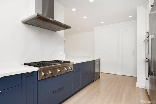 kitchen featuring appliances with stainless steel finishes, crown molding, wall chimney range hood, light hardwood / wood-style floors, and wine cooler