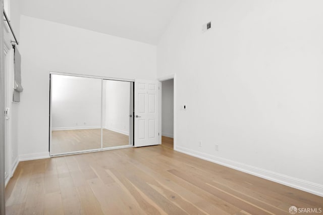 unfurnished bedroom with a closet, high vaulted ceiling, and light hardwood / wood-style floors