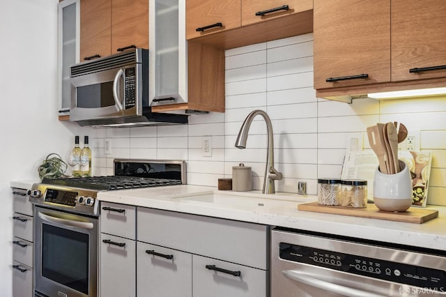 kitchen featuring stainless steel appliances, light stone counters, tasteful backsplash, and sink