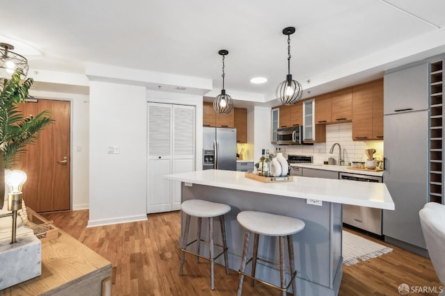 kitchen with decorative light fixtures, stainless steel appliances, light wood-type flooring, and a breakfast bar