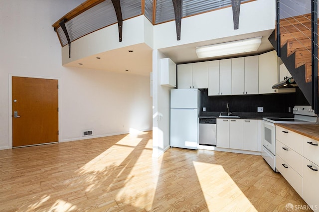 kitchen featuring white appliances, a high ceiling, white cabinets, sink, and light hardwood / wood-style flooring