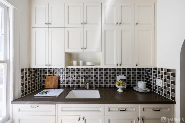 kitchen with a sink, dark countertops, white cabinets, and tasteful backsplash