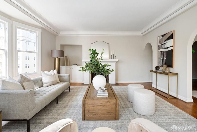 living room with wood finished floors, arched walkways, ornamental molding, and baseboards