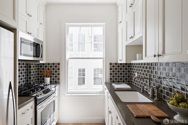 kitchen with appliances with stainless steel finishes, a sink, dark countertops, and decorative backsplash