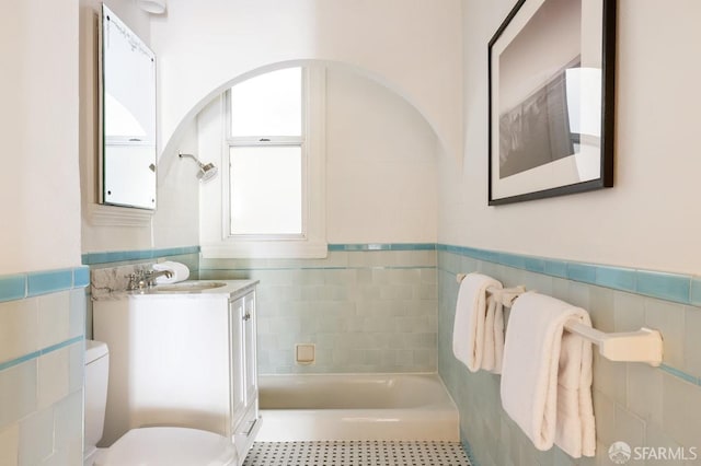 full bathroom featuring tile walls, toilet, tile patterned flooring, a wainscoted wall, and a tub