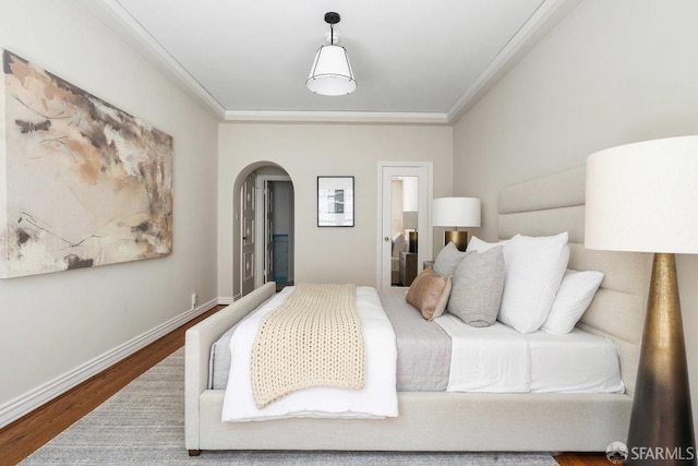bedroom featuring wood finished floors, arched walkways, baseboards, and ornamental molding