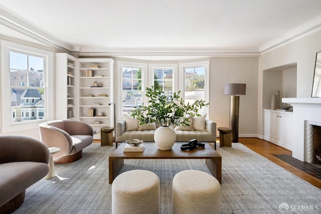 living area with ornamental molding, a tile fireplace, wood finished floors, and baseboards