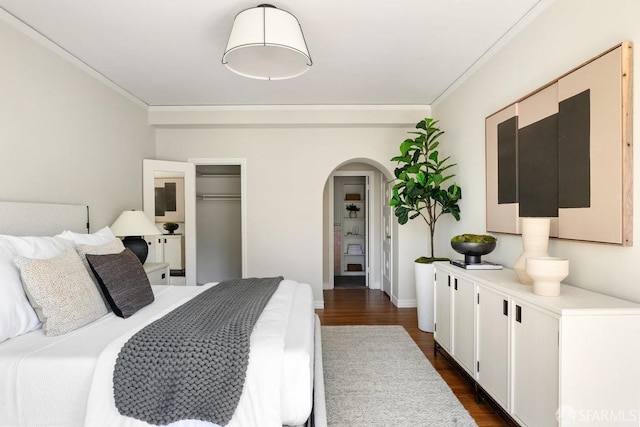 bedroom with arched walkways, dark wood-style flooring, crown molding, baseboards, and a closet