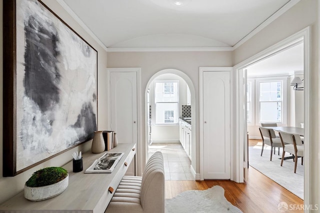 corridor featuring vaulted ceiling, light wood finished floors, arched walkways, baseboards, and crown molding