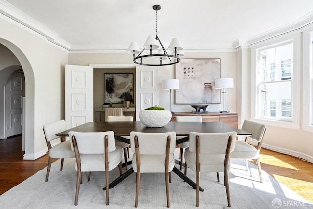 dining space with a chandelier, crown molding, wood finished floors, arched walkways, and baseboards