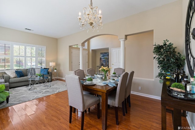 dining area featuring ornate columns, wood-type flooring, and a notable chandelier