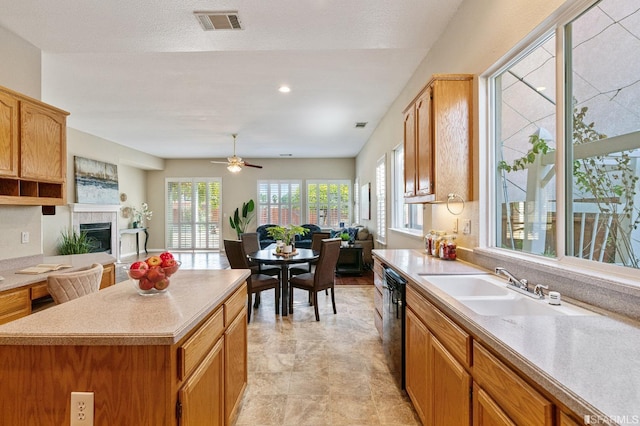 kitchen featuring sink, dishwasher, a kitchen island, ceiling fan, and a fireplace