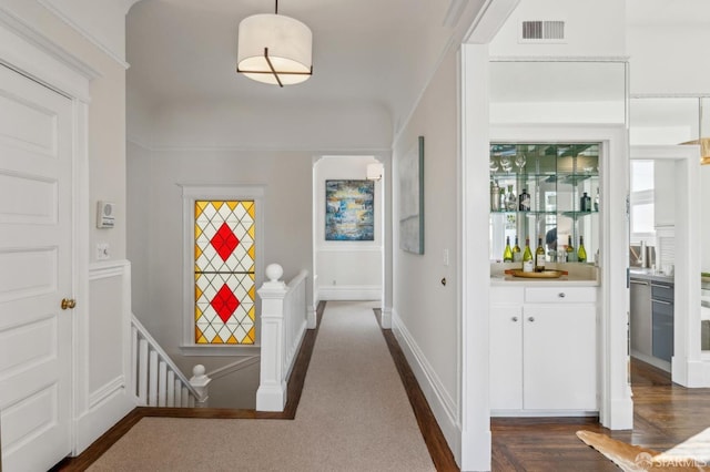 hall with dark wood-style floors, an upstairs landing, visible vents, and baseboards