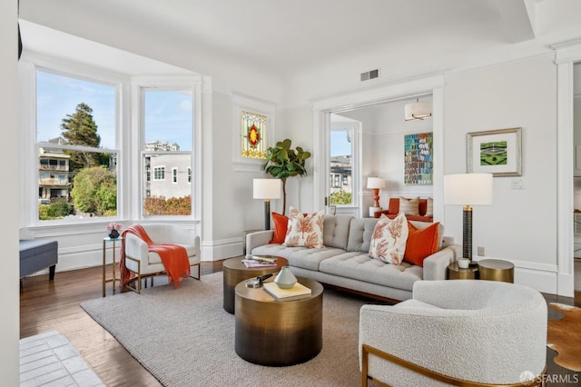 living room featuring visible vents, plenty of natural light, baseboards, and wood finished floors