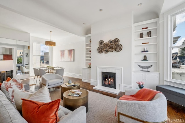 living room with dark wood-type flooring, built in shelves, a fireplace, and baseboards