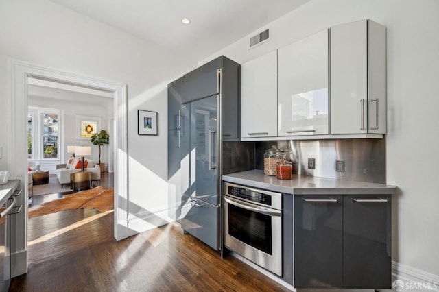 kitchen featuring visible vents, modern cabinets, backsplash, stainless steel oven, and dark wood-style flooring