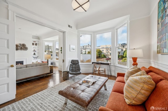 living room with built in features, a warm lit fireplace, visible vents, and wood finished floors