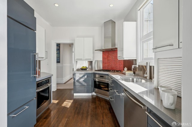 kitchen featuring a sink, wall chimney range hood, stainless steel appliances, white cabinetry, and modern cabinets