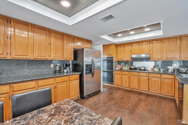 kitchen with black appliances, a tray ceiling, ornamental molding, dark hardwood / wood-style floors, and decorative backsplash