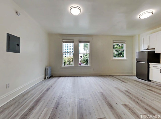 interior space featuring electric panel, light hardwood / wood-style flooring, and radiator heating unit