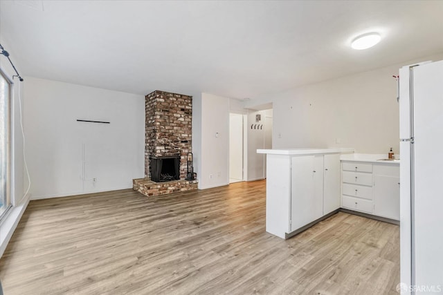 kitchen with white cabinetry, a brick fireplace, white fridge, light wood-type flooring, and kitchen peninsula