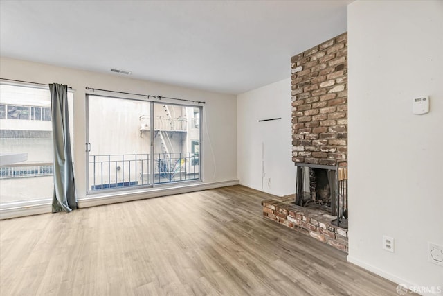 unfurnished living room featuring hardwood / wood-style flooring, a brick fireplace, and a healthy amount of sunlight