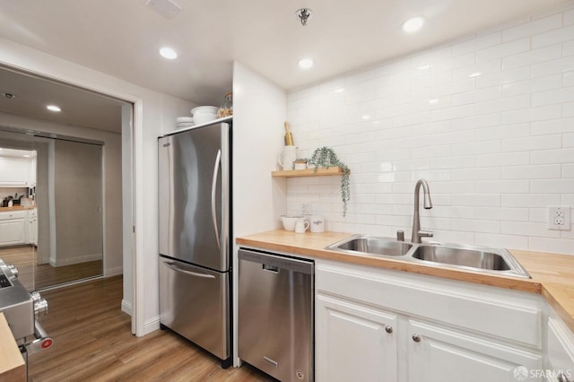 kitchen with wooden counters, appliances with stainless steel finishes, decorative backsplash, white cabinets, and sink