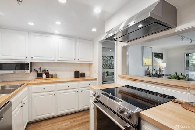 kitchen with white cabinets, appliances with stainless steel finishes, butcher block countertops, and range hood