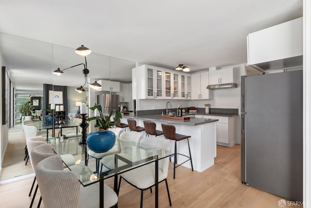 kitchen with freestanding refrigerator, glass insert cabinets, light wood-type flooring, and dark countertops