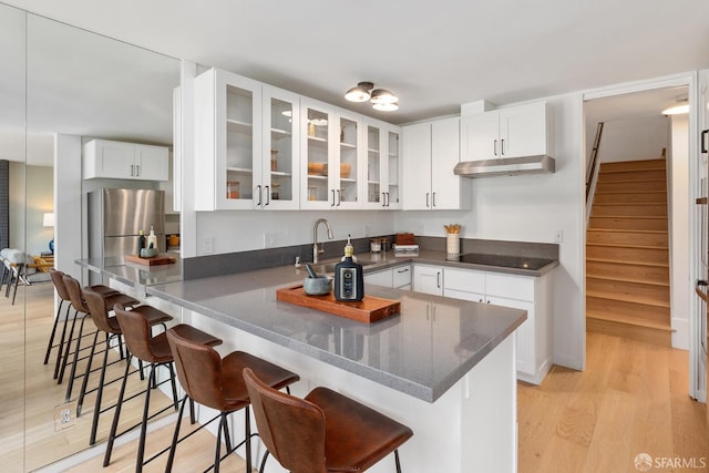 kitchen with a peninsula, a kitchen breakfast bar, glass insert cabinets, light wood finished floors, and white cabinetry