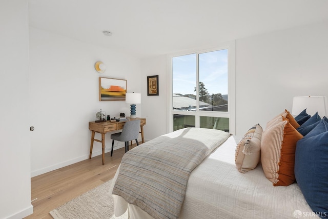 bedroom with light wood finished floors, floor to ceiling windows, and baseboards