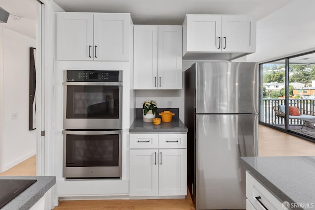 kitchen featuring stainless steel appliances, white cabinetry, light wood-style floors, and dark stone counters