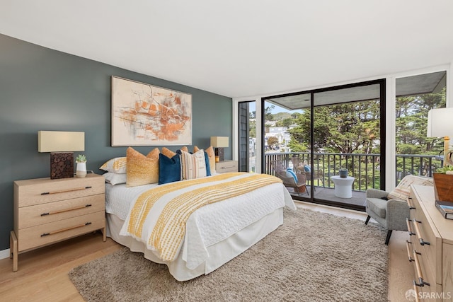 bedroom with access to outside, a wall of windows, light wood-type flooring, and baseboards