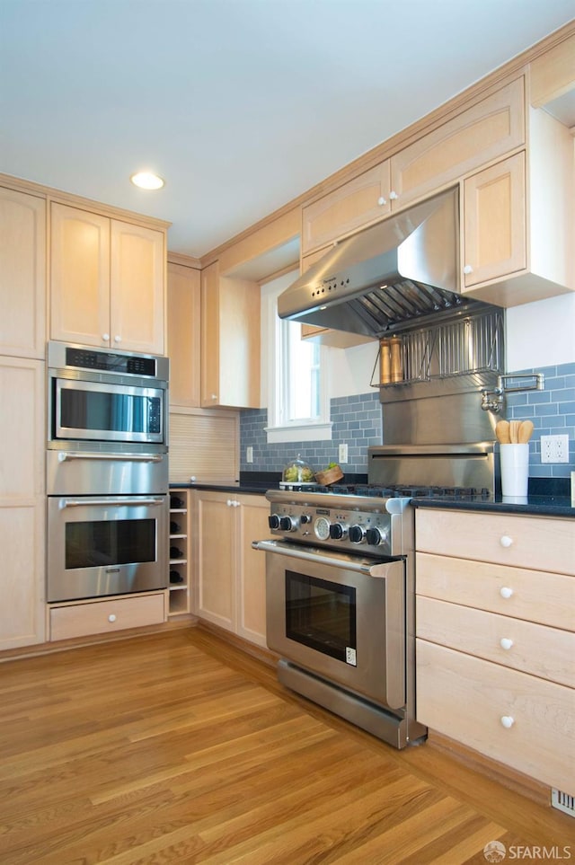 kitchen with light brown cabinets, under cabinet range hood, backsplash, stainless steel appliances, and light wood finished floors