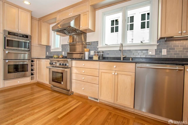 kitchen with light brown cabinets, under cabinet range hood, tasteful backsplash, stainless steel appliances, and light wood-style floors