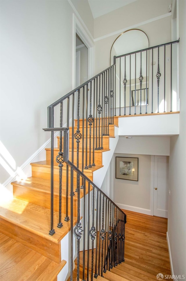 stairway with baseboards, a high ceiling, and wood finished floors