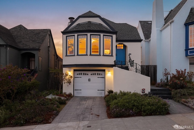 view of front of house with stucco siding, roof with shingles, and driveway