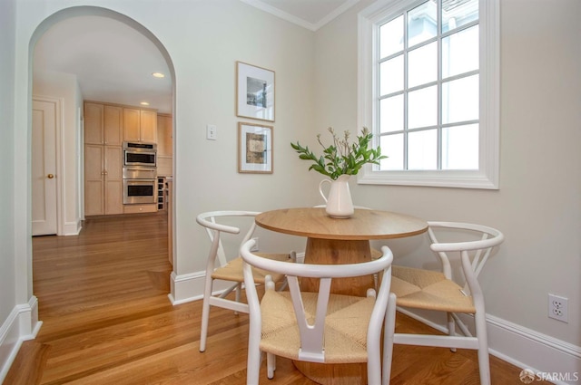 dining space featuring a wealth of natural light, baseboards, arched walkways, and light wood-style floors