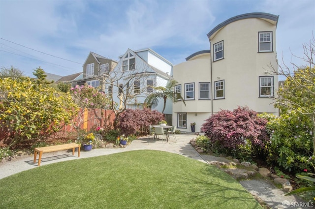 rear view of property featuring stucco siding, fence, a yard, and a patio area