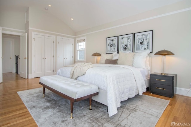 bedroom featuring baseboards, light wood finished floors, lofted ceiling, recessed lighting, and multiple closets