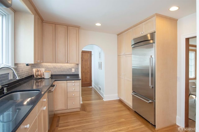 kitchen with backsplash, light brown cabinets, light wood-type flooring, arched walkways, and stainless steel appliances