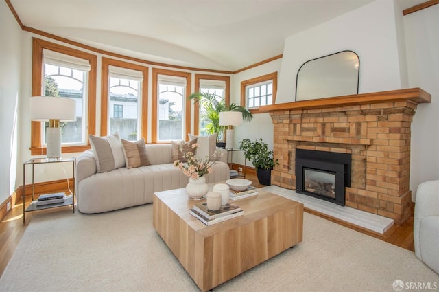 living area featuring crown molding, a fireplace, light wood-type flooring, and vaulted ceiling