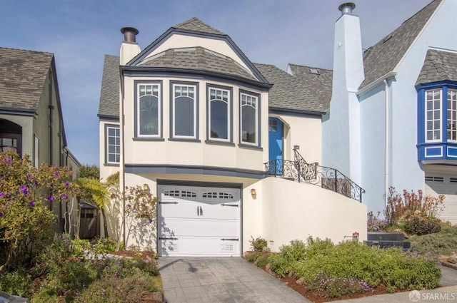 view of front of house with stucco siding, decorative driveway, roof with shingles, an attached garage, and a chimney