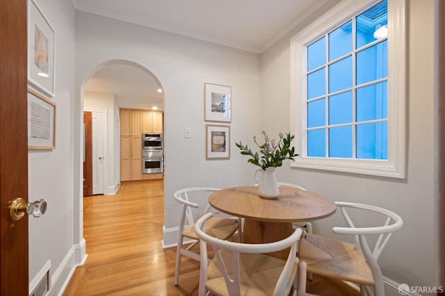 dining space featuring light wood-style flooring, baseboards, and arched walkways