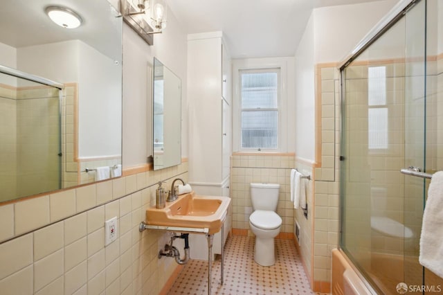 bathroom featuring shower / bath combination with glass door, toilet, and tile walls