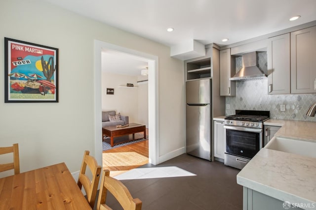 kitchen featuring wall chimney exhaust hood, sink, gray cabinetry, stainless steel appliances, and backsplash