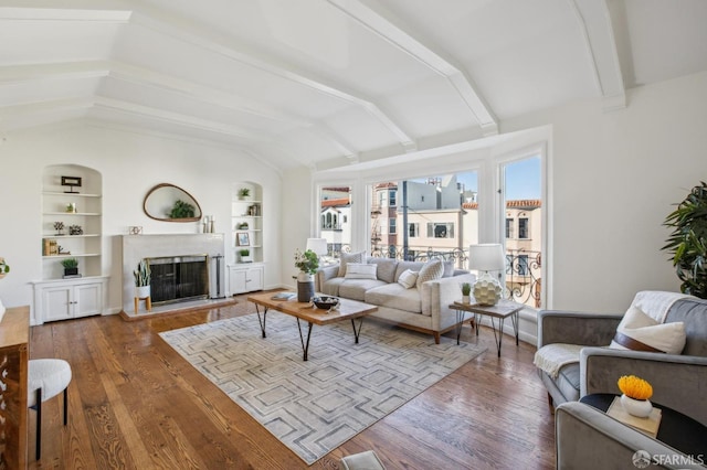 living room with built in shelves, wood-type flooring, and vaulted ceiling with beams