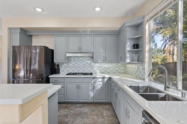 kitchen featuring range hood, tasteful backsplash, sink, gray cabinetry, and stainless steel appliances