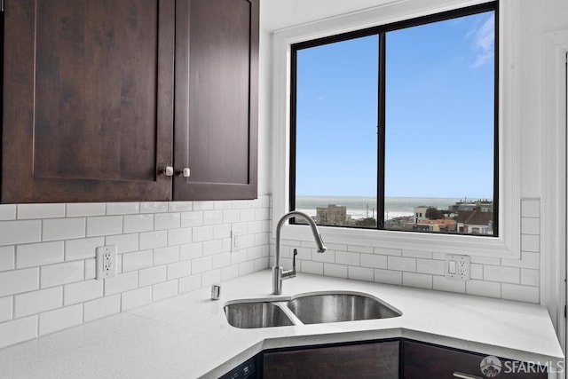 kitchen with dark brown cabinets, tasteful backsplash, a sink, and light countertops